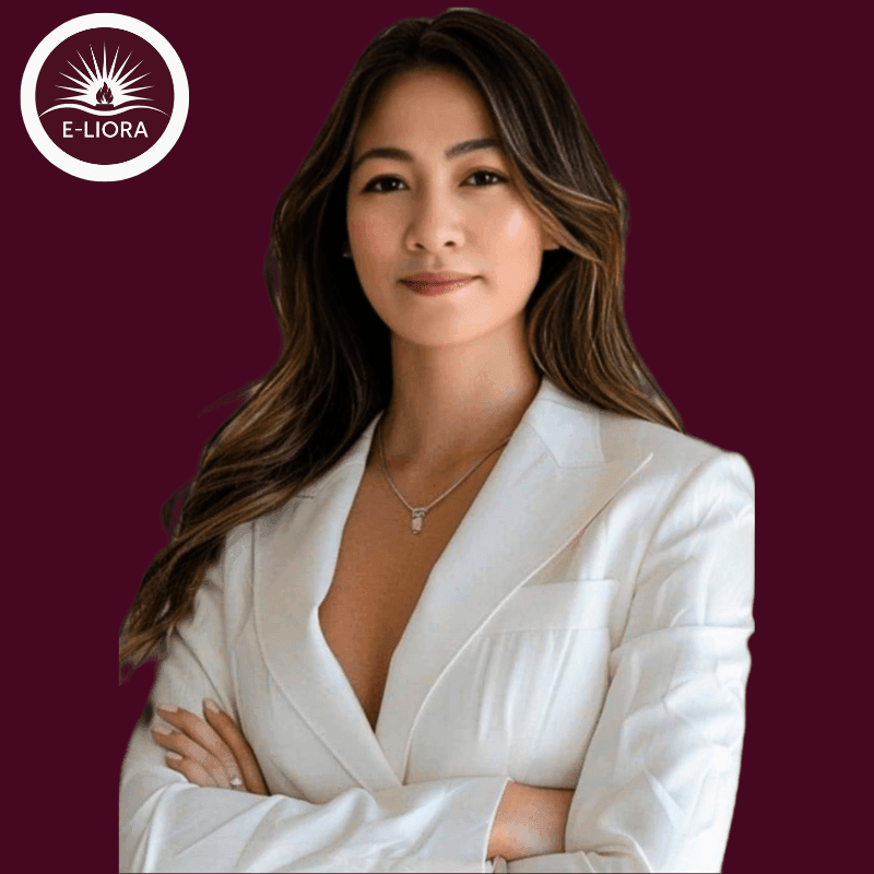 Woman wearing white blazer and necklace with arms crossed, E-Liora logo in top left corner.