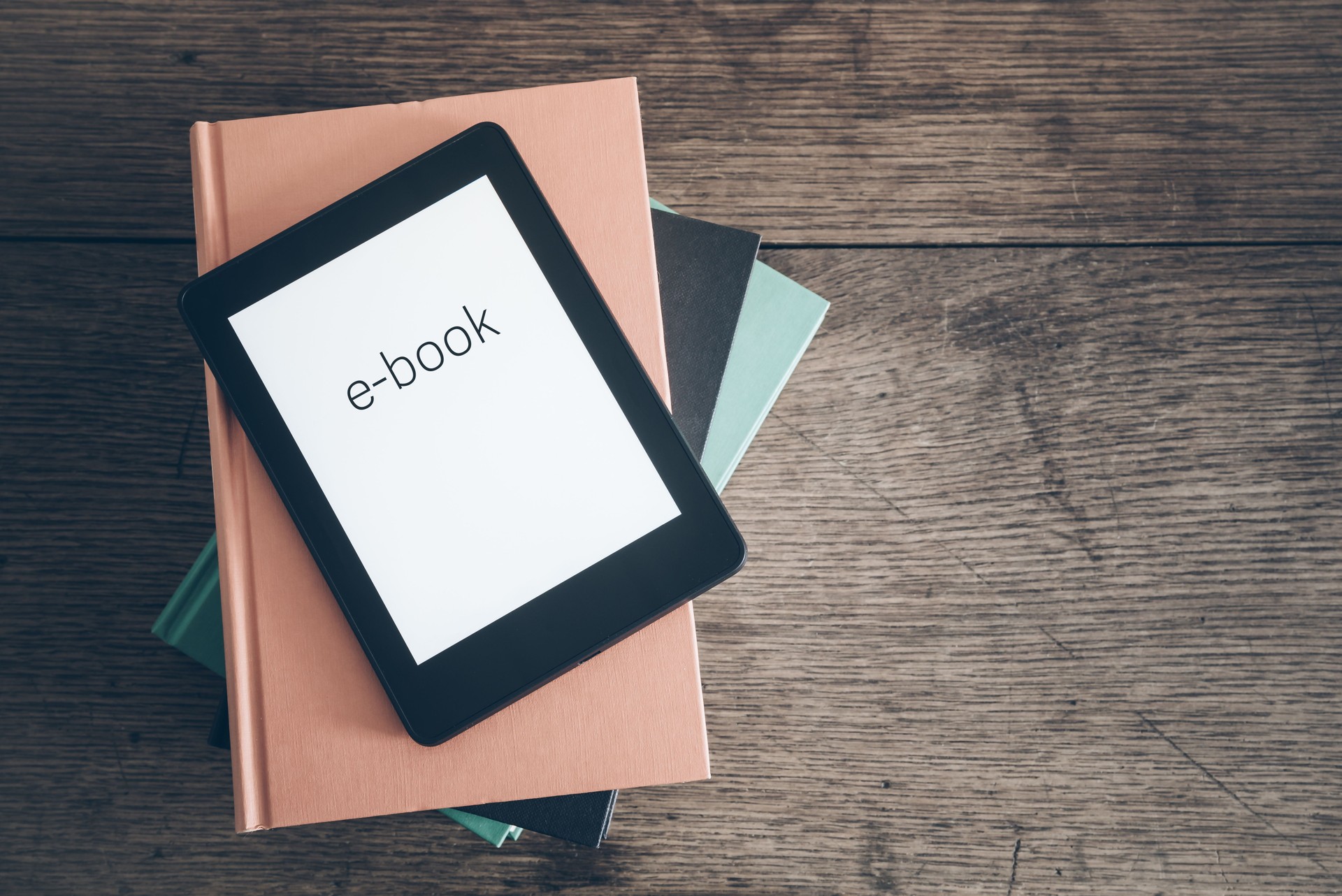 e-book reader on a stack of books on rustic wooden table concept